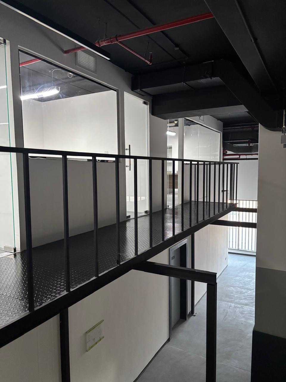 Industrial mezzanine with black metal walkway, glass-walled offices, and exposed ceiling services